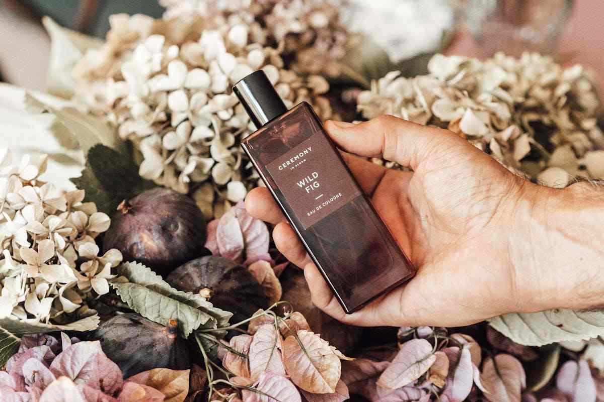 Mano che stringe boccetta di profumo. Fiori sullo sfondo
