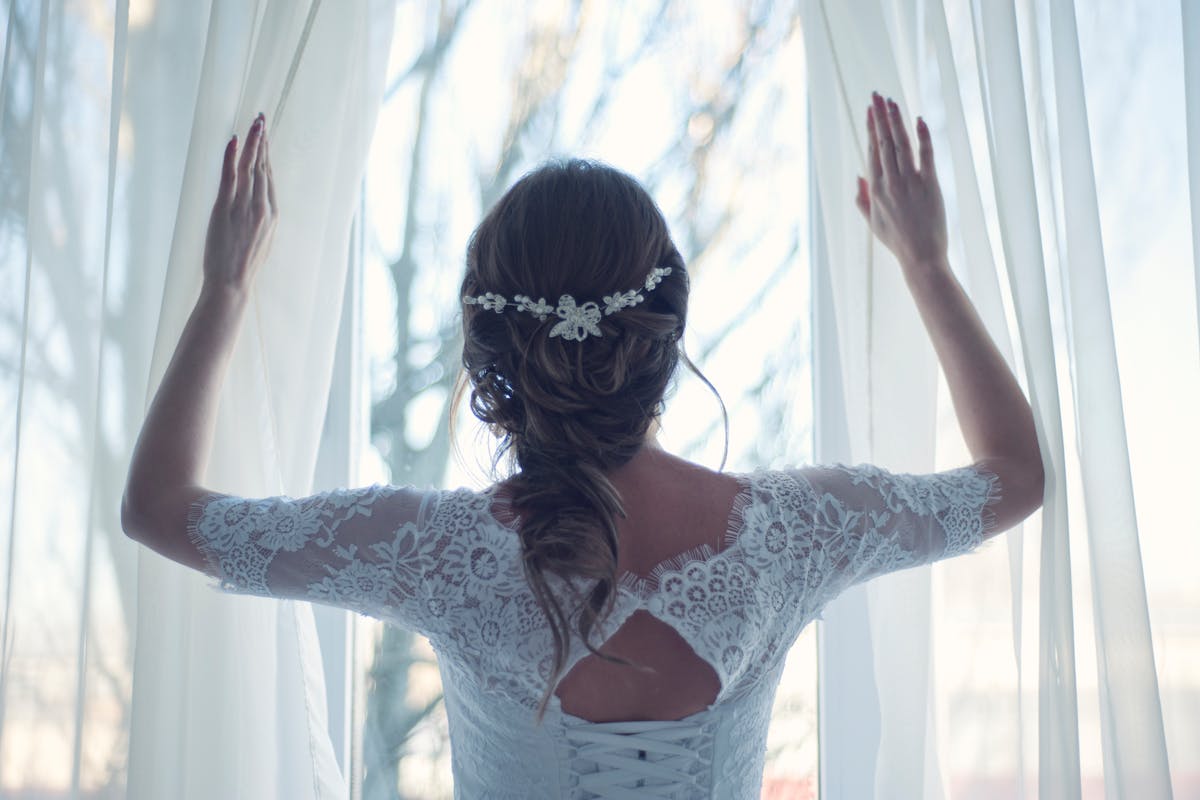 donna vestita da sposa di spalle che apre le tende