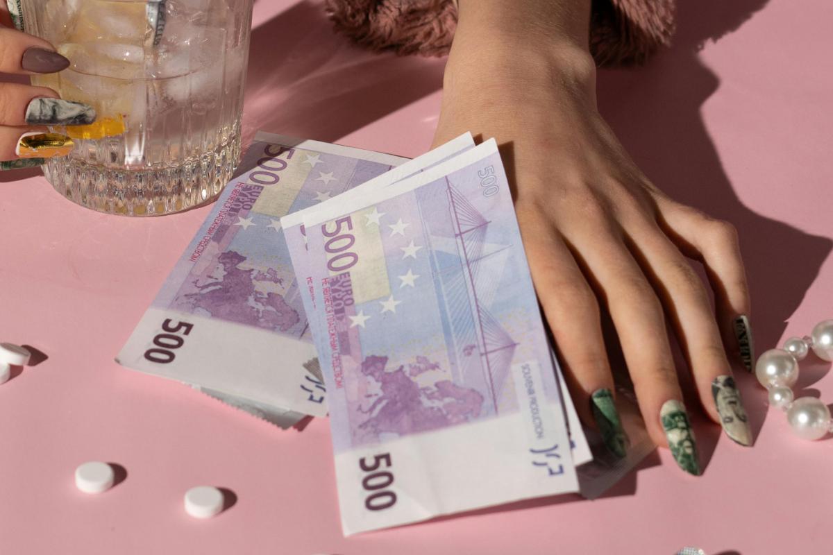 Banconote da 500 euro su un tavolo rosa, con una mano con le unghie lunghe