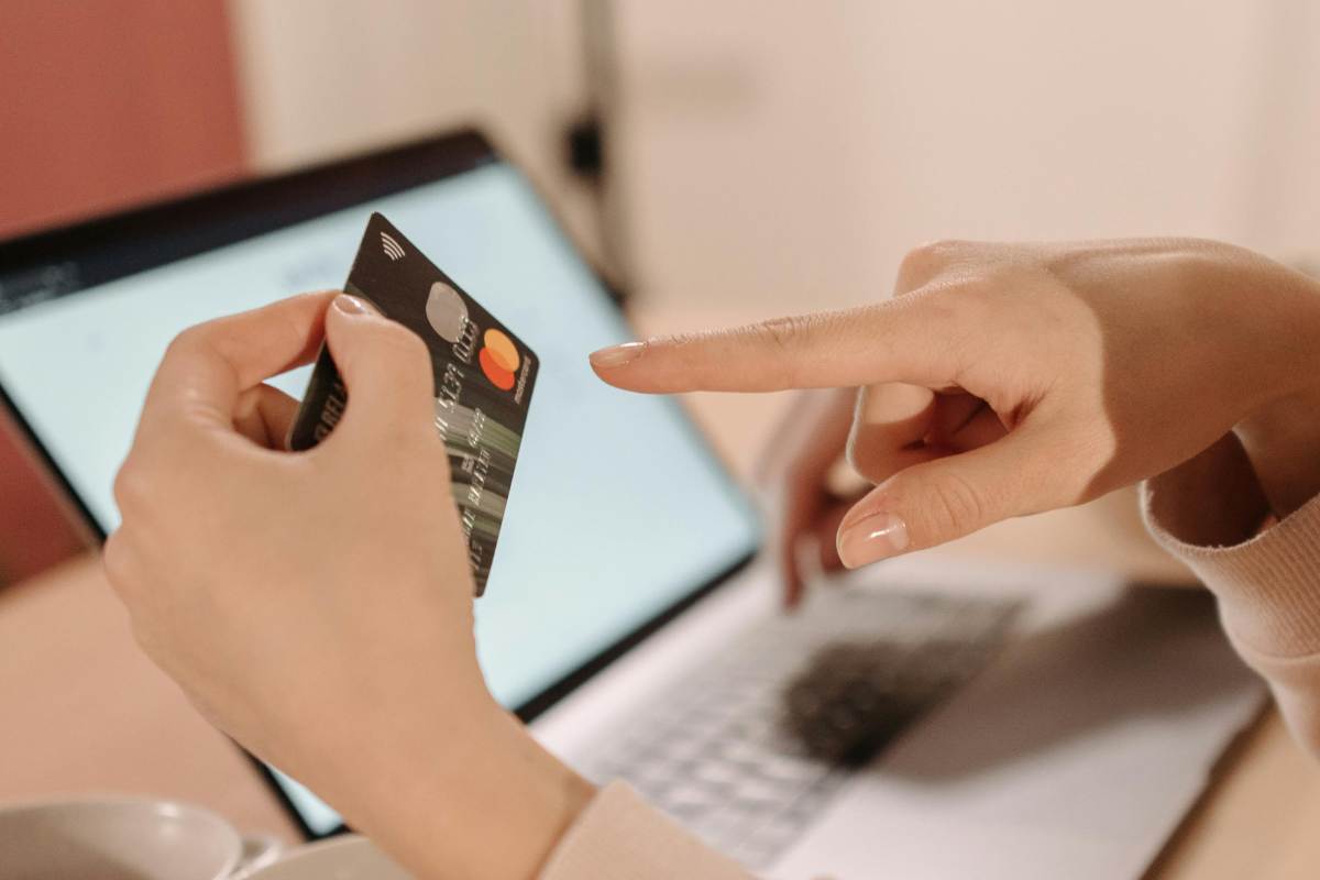 Una mano che indica una carta di credito e, sullo sfondo, un laptop