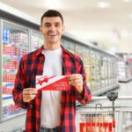 Un uomo con un buono pasto accanto ad un carrello al supermercato