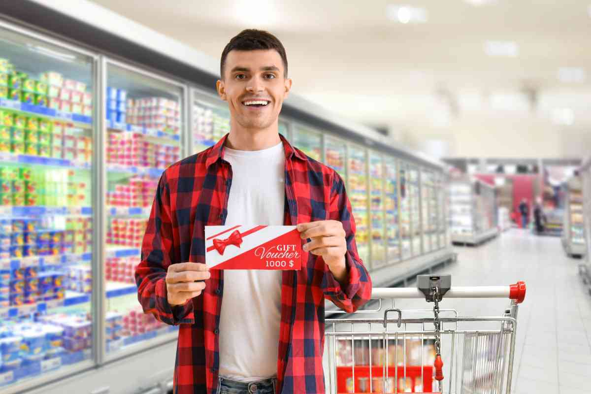 Un uomo con un buono pasto accanto ad un carrello al supermercato