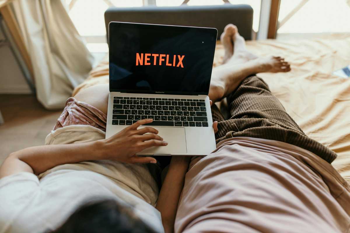 coppia sdraiata a letto guarda un film Netflix sul pc portatile