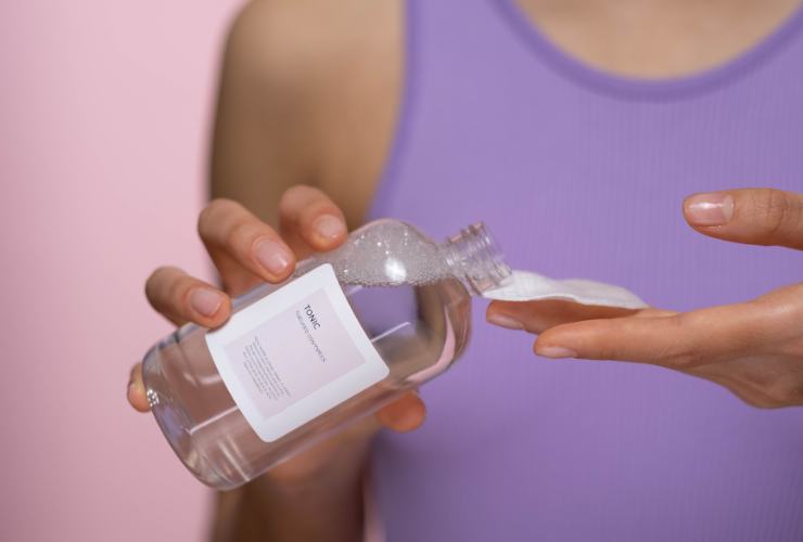 Donna che versa il tonico sul dischetto struccante