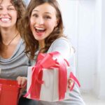 due ragazze sorridenti porgono un regalo a chi guarda