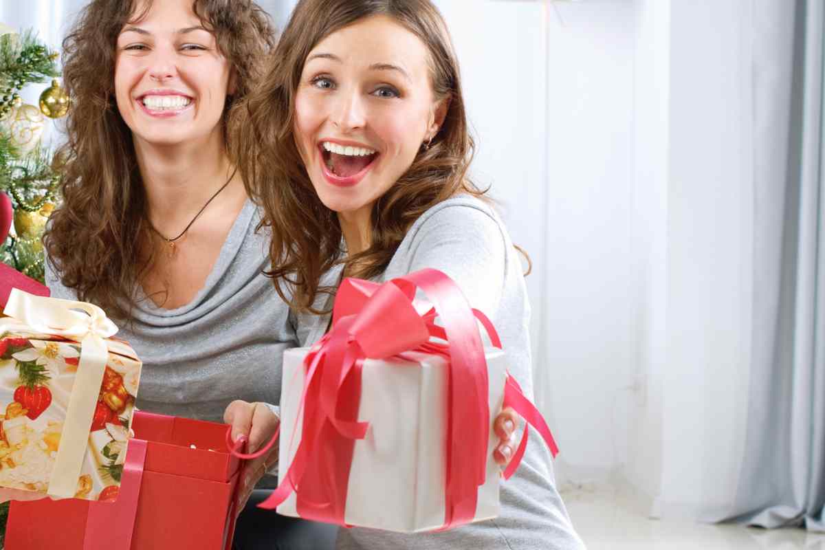 due ragazze sorridenti porgono un regalo a chi guarda