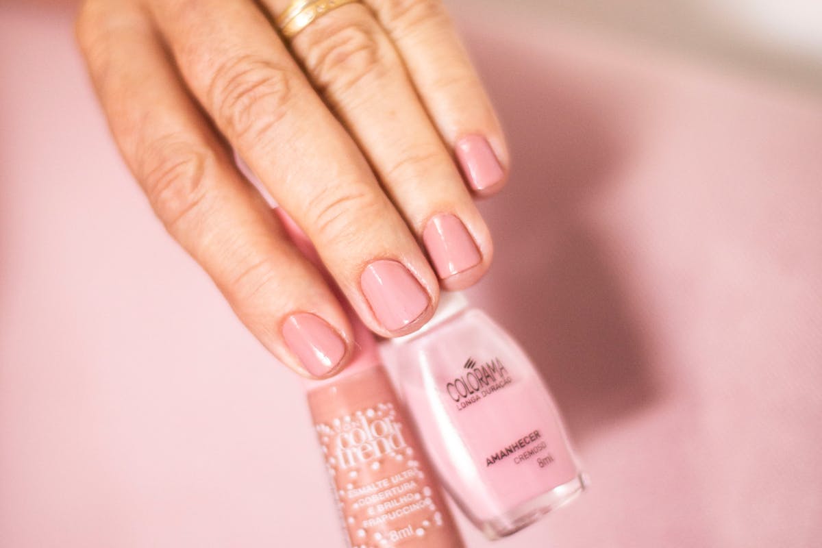 mano con unghie rosa che stringe due smalti