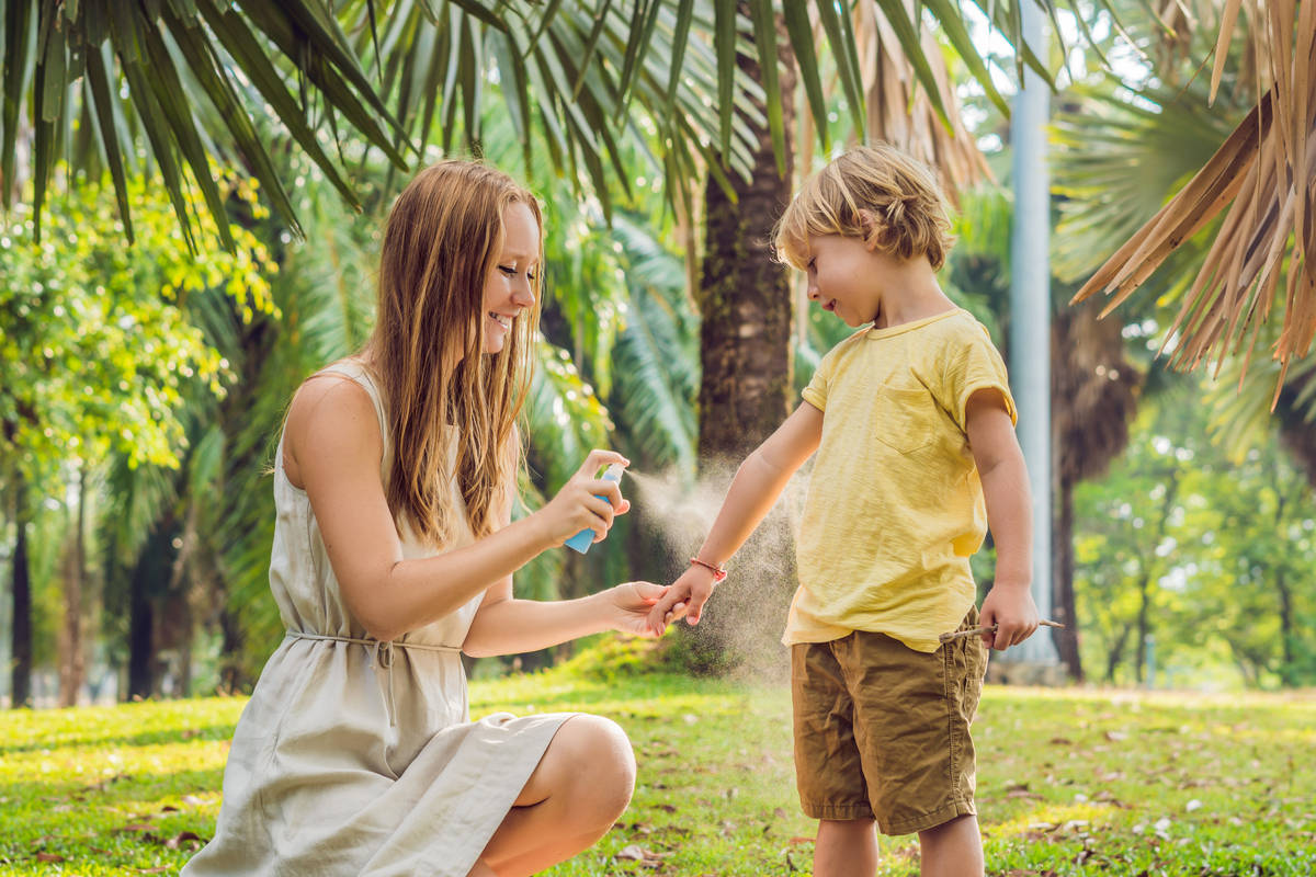 Mamma che mette lo spray anti insetti al figlio