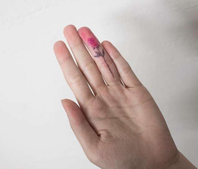 Tatuaggio colorato rosa rossa su un dito